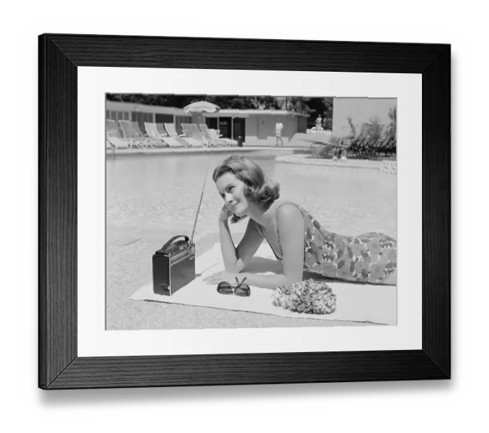 Framed Print : Woman lying on towel poolside listening to radio with antenna up