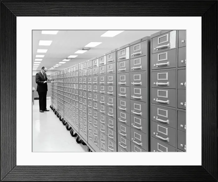 Framed Print : Row of metal filing cabinets on casters, man standing at end of row, with drawer open Framed Print : Row of metal filing cabinets on casters, man standing at end of row, with drawer open