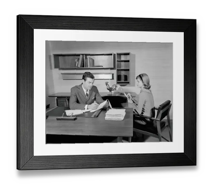 Framed Print : Businessman sitting at desk reading papers, secretary taking notes Framed Print : Businessman sitting at desk reading papers, secretary taking notes