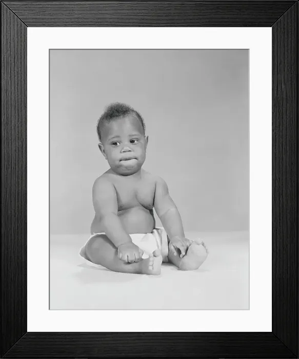 Framed Print : African-American baby sitting with hands on legs, biting lower lip, portrait Framed Print : African-American baby sitting with hands on legs, biting lower lip, portrait