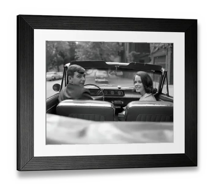 Framed Print : Couple in convertible, smiling, looking over shoulders, portrait Framed Print : Couple in convertible, smiling, looking over shoulders, portrait