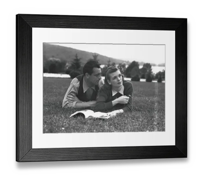 Framed Print : Couple with magazine, lying on grass, (B&W) Framed Print : Couple with magazine, lying on grass, (B&W)