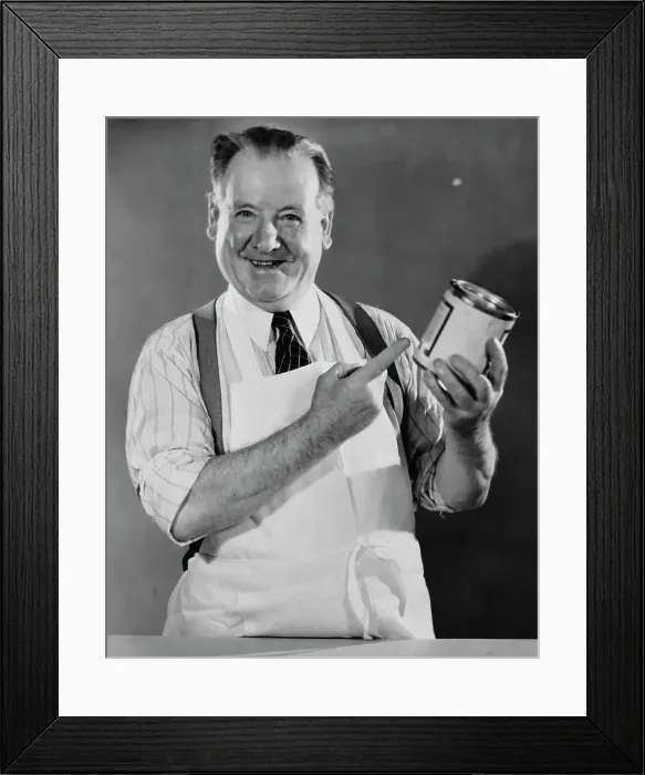 Framed Print : Grocer. A shopkeeper with a tin of food, circa 1940