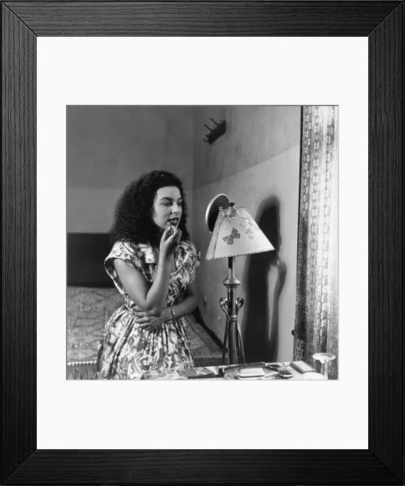 Framed Print : Tiger Bay. A woman applying lipstick in front of a mirror at home in Tiger