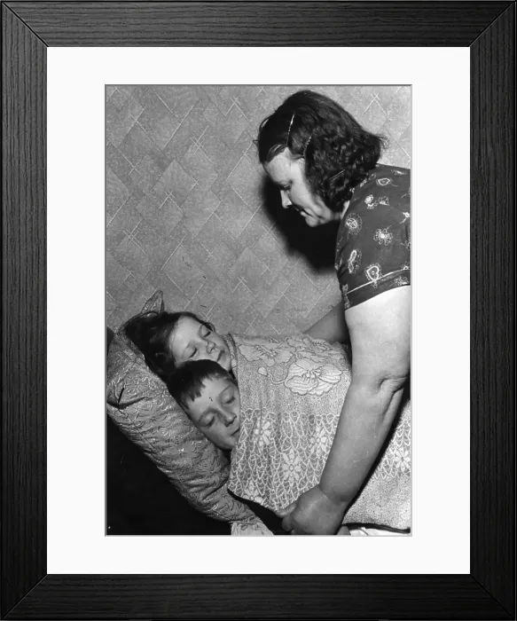 Framed Print : Bedtime. 30th November 1940: A woman putting her children to bed in cramped slum housing Framed Print : Bedtime. 30th November 1940: A woman putting her children to bed in cramped slum housing