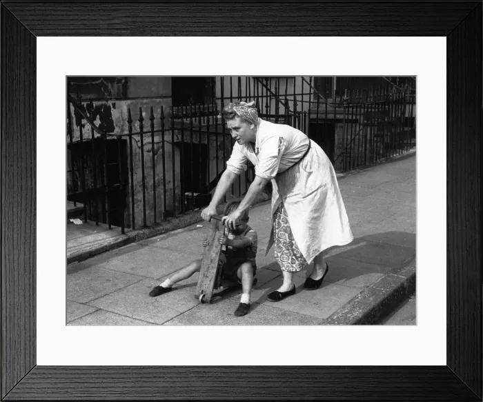 Framed Print : Scooter. 7th August 1954: A mother pushes her child along the street on its scooter Framed Print : Scooter. 7th August 1954: A mother pushes her child along the street on its scooter