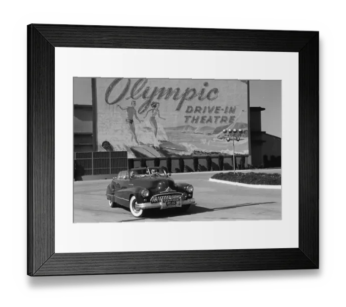 Framed Print : Drive-In. Two women in an open-top car driving past a sign advertising Framed Print : Drive-In. Two women in an open-top car driving past a sign advertising
