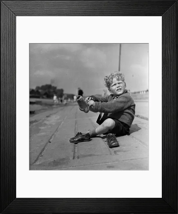 Framed Print : Sore Feet. 25th June 1949: A young lad takes off his shoes in the middle Framed Print : Sore Feet. 25th June 1949: A young lad takes off his shoes in the middle