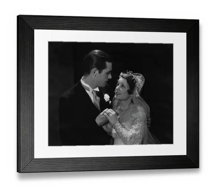 Framed Print : Love Is. A groom and bride, her veil lifted, in a black suit