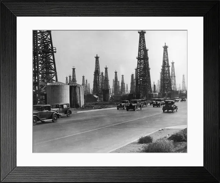 Framed Print : Oil Field. circa 1930: Derricks stand behind traffic on a highway at the Framed Print : Oil Field. circa 1930: Derricks stand behind traffic on a highway at the