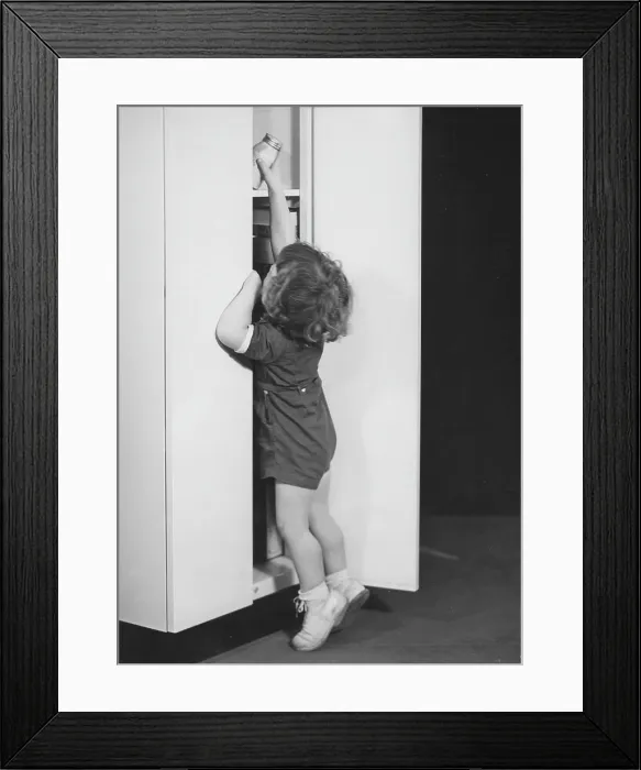 Framed Print : Larder. A young girl reaching up to grab a jar from the larder, circa 1940s