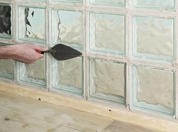 Adding grout to joints around a glass block with a trowel