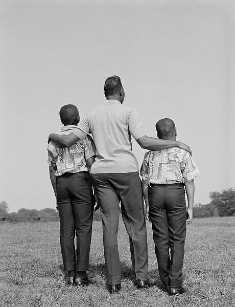 African-American father with arms around two sons, rear view