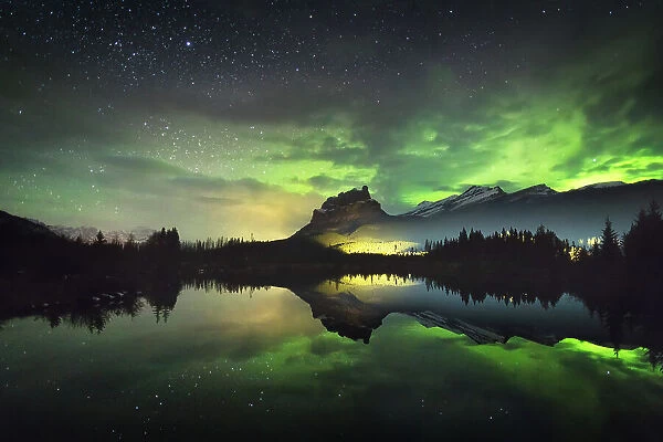 The aurora reflected in a small lake below Castle Mountain as a train light goes by, Banff National Park, Alberta, Canada