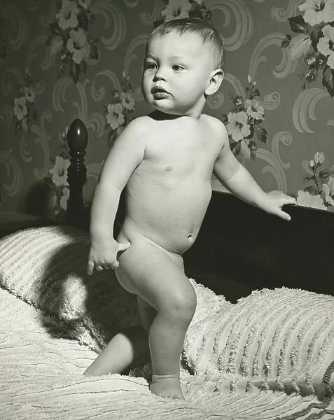 Baby (12-15 months) standing on bed, (B&W)