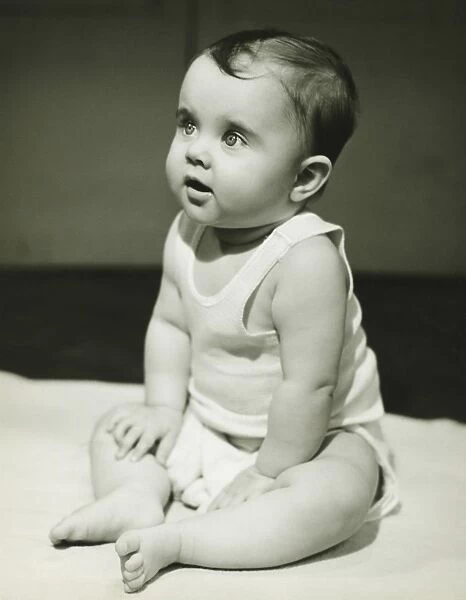Baby boy (12-18 months) sitting on bedspread, (B&W), close-up