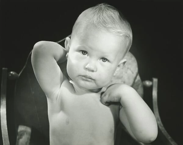 Baby boy (6-12 months) sitting in high chair, (B&W), portrait