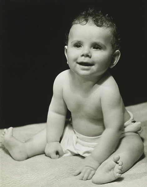 Baby boy (6-9 months) in nappy sitting on blanket, (B&W), portrait