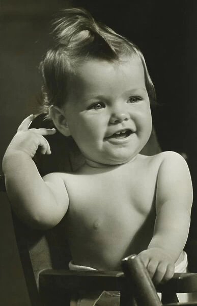 Baby boy (6-9 months) sitting in high chair, (B&W), portrait