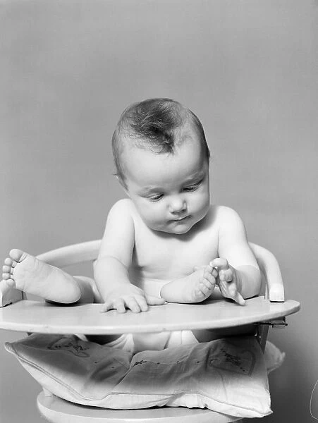 Baby with feet propped up on highchair tray, playing with toes