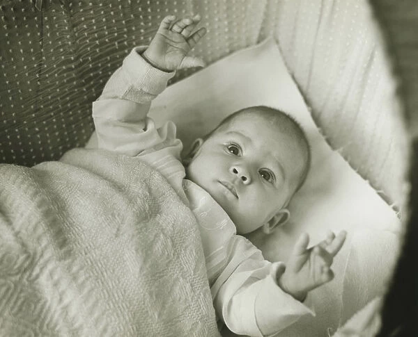Baby girl (6-12 months) lying in bed with arms raised, (B&W)