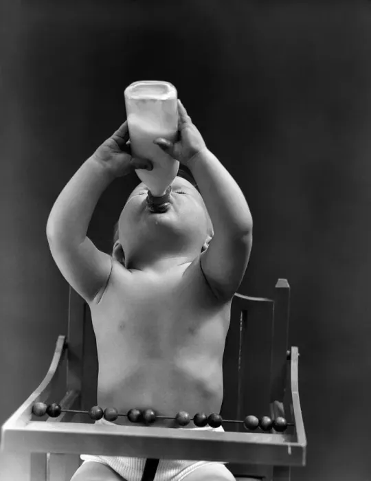 Framed Print : Baby sitting in high chair, head tilted back, drinking from milk bottle. (Photo by H Framed Print : Baby sitting in high chair, head tilted back, drinking from milk bottle. (Photo by H