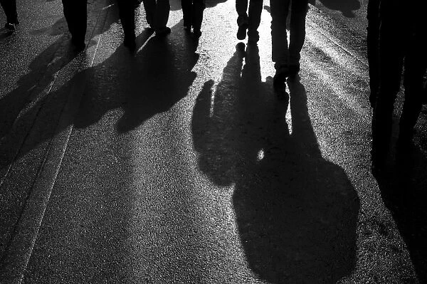 Backlit persons casting shadows on the asphalt