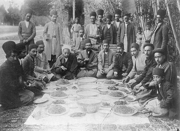 Banquet. circa 1910: A Persian dinner party with food laid out on a carpet on the ground