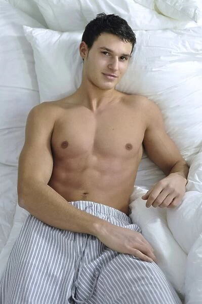 Bare-chested young man wearing pyjama bottoms lying in bed