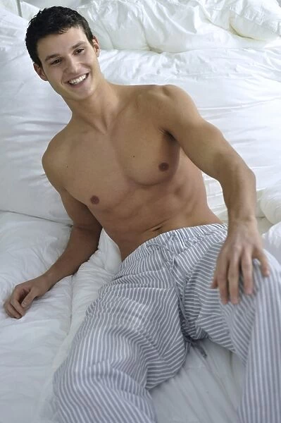Bare-chested young man wearing pyjama bottoms lying in bed