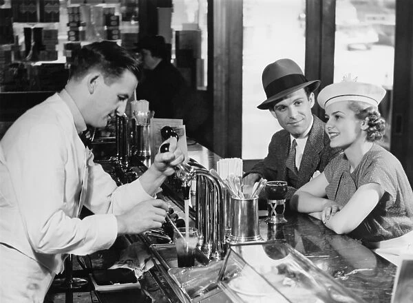 Bartender pouring beer for young couple in bar, (B&W)