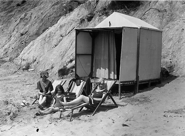 Beach Hut. circa 1930: Two women and a child sunbathing outside their hut on the beach