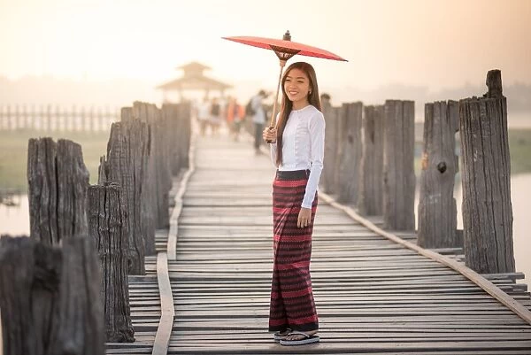 Beautiful woman holding traditional red umbrella and walking on U Bein Bridge, Myanmar