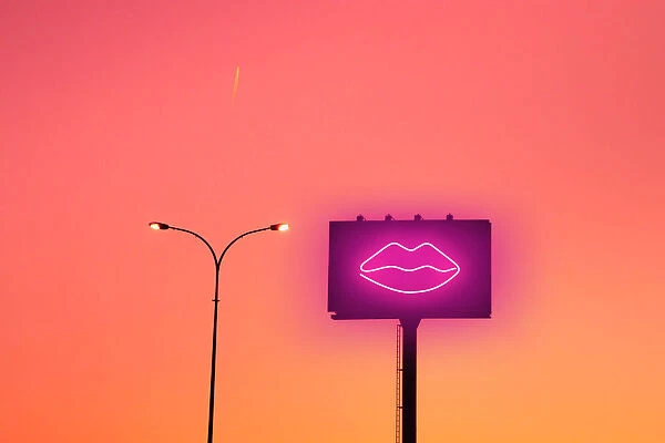 Billboard with sexy lips neon light and sunset sky in the city