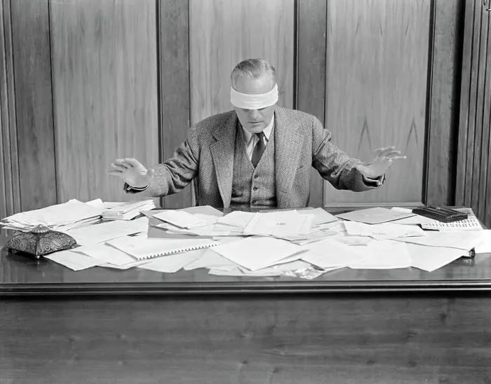 Framed Print : Blindfolded Businessman At Desk Covered With Papers Framed Print : Blindfolded Businessman At Desk Covered With Papers