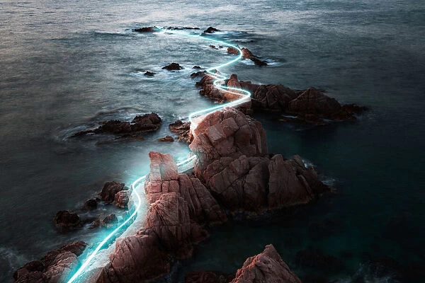 Blue light trail following footpath between the stunning coastline during sunrise