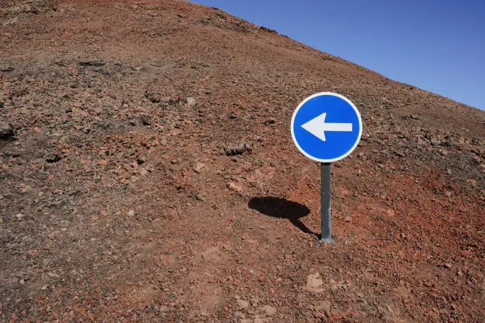 Framed Print : Blue sign with a white arrow pointing left, on red lava, Lanzarote, Canary Islands, Spain