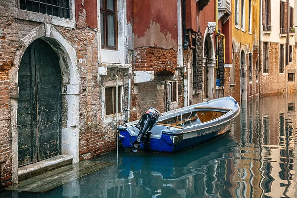 Boat moored by the townhouse door facing canal in Venice, Italy