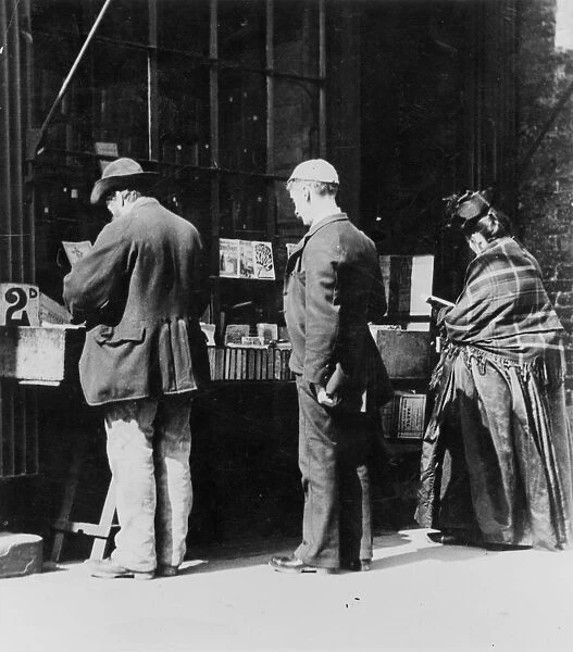 Bookstall. circa 1900: Customers browsing through some books at a bookstall
