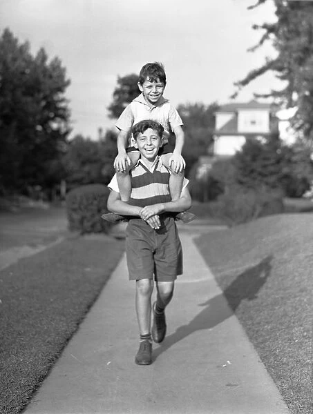 Boy (10-11) carrying brother (6-7) on shoulders, (B&W), portrait