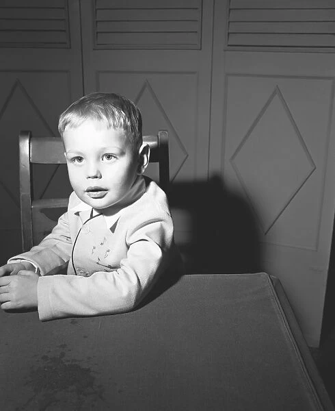 Boy (3-4) sitting at table, (B&W), portrait
