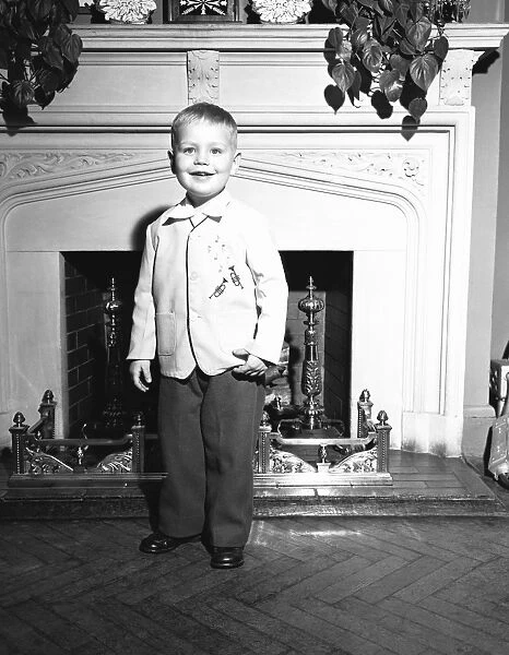 Boy (3-4) standing by fireplace, (B&W), portrait