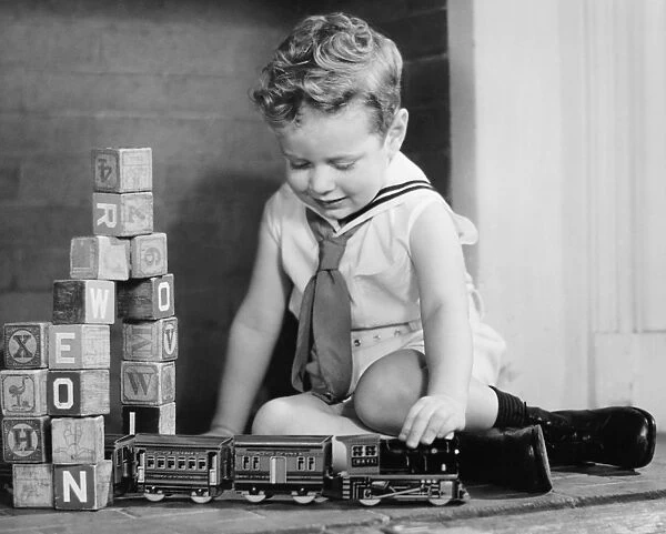Boy (4-5) playing with model train set on floor, (B&W)