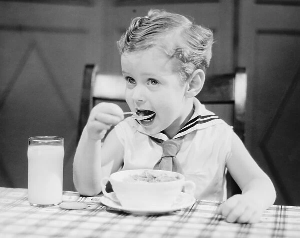 Boy (4-5) wearing sailor suit, eating at table, (B&W), portrait