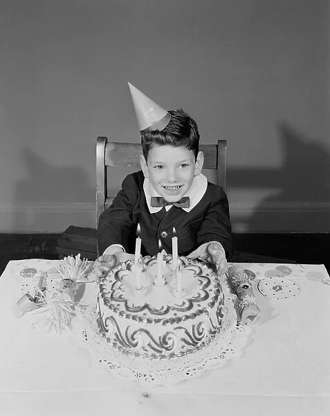 Boy (6-7) sitting at table with birthday cake, portrait