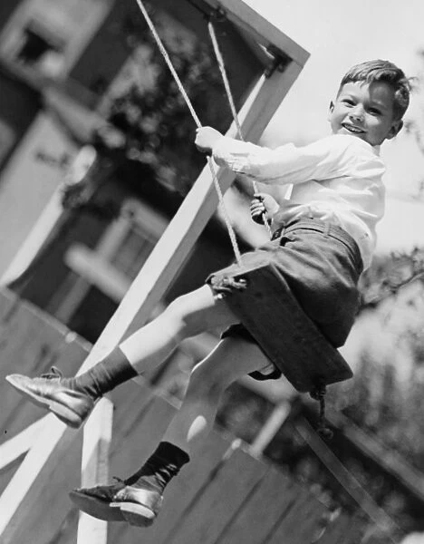 Boy (6-7) swinging in garden, (B&W), (Low angle view)
