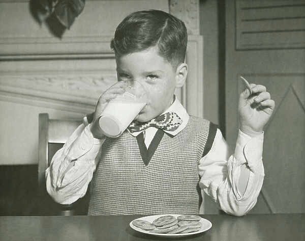Boy (8-9) drinking glass of milk, sitting at table, (B&W), close-up