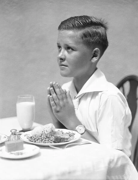Boy at dinner table, saying Grace
