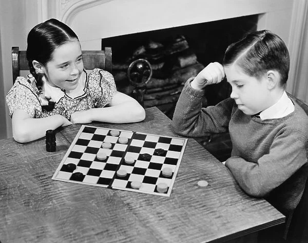 Boy and girl (8-9) playing checkers (B&W), elevated view