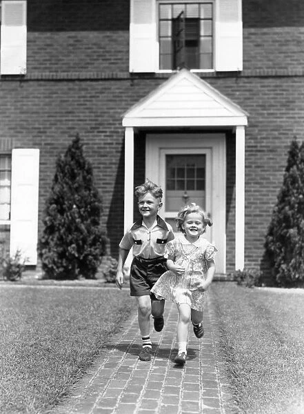Boy and girl running on sidewalk in front of house